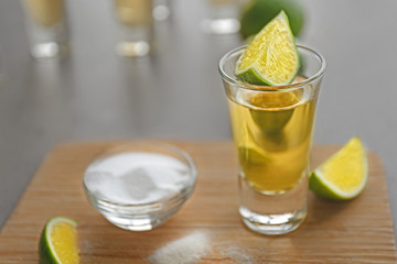 Shot of gold tequila with lime slices and salt on wooden board