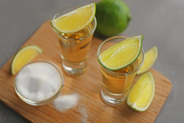 Shots of gold tequila with lime slices and salt on wooden board