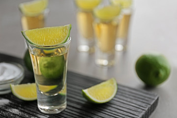 Shot of gold tequila with lime slices and salt on wooden board