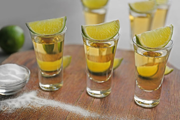 Shots of gold tequila with lime slices and salt on wooden board