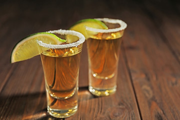 Gold tequila shots with lime slices and salt on wooden background