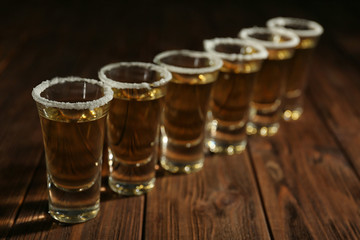 Gold tequila shots in a row with salt on wooden background