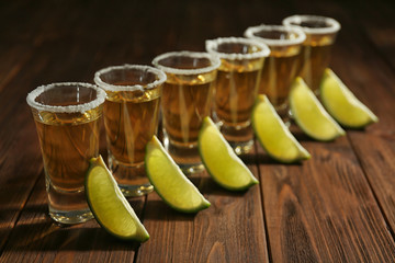 Gold tequila shots in a row with lime slices and salt on wooden background