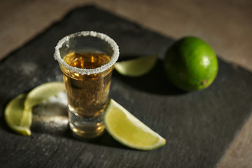 Gold tequila shot with lime on grey board