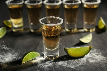 Shots of gold tequila with lime slices and salt on grey background