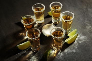 Shots of gold tequila with lime slices and salt on grey background