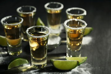 Shots of gold tequila with lime slices and salt on grey background
