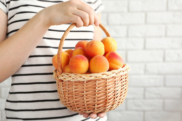 Woman holding heap of apricots in wicker basket, closeup