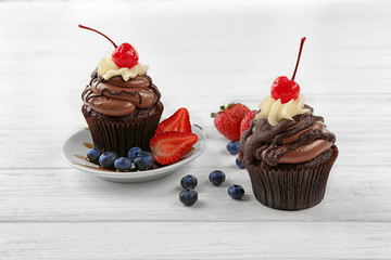 Delicious chocolate cupcakes with berries on white table