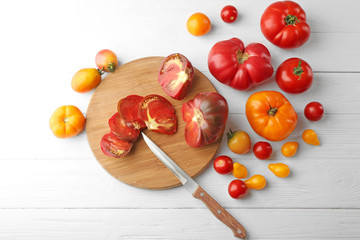 Composition of tomatoes, knife and cutting board on white wooden background