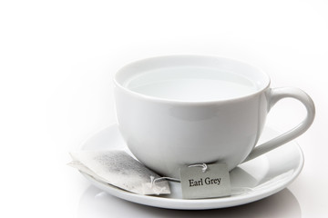 White cup and saucer with an earl grey tea bag on a white backgr