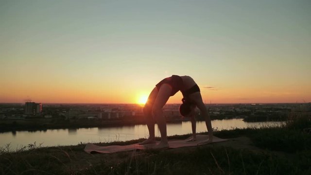 Silhouette of sporty woman practicing yoga in the park at sunset - drop back, wheel pose. Sunset light, sun lens flares, golden hour. Freedom, health and yoga concept