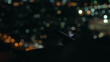 Night cityscape with following close-up shot of the woman typing on mobile phone against blurred city lights - Powered by Adobe