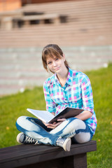 Student girl with copybook on bench outdoor. Summer campus park. Studying to exam.