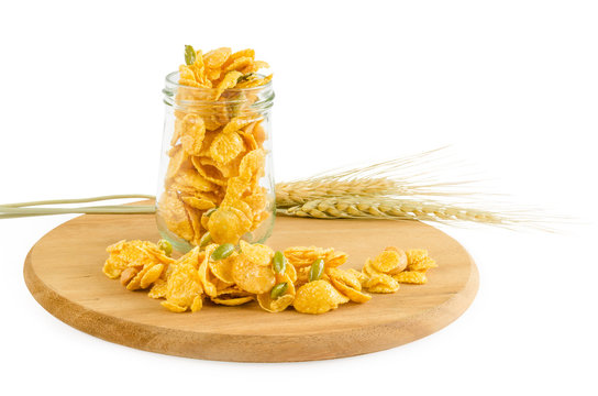 Fresh homemade caramel corn flakes cereal with sun flower seeds in clear glass bottle or container over wooden tray with dried wheat barley isolated on white background