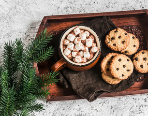 Hot chocolate with marshmallows and chocolate chips oatmeal cookies on wooden tray on a bright background