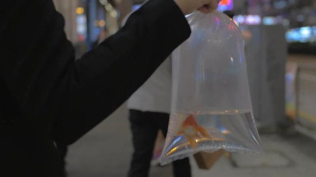 Slow motion shot of a woman in the street walking with fish in plastic bag. Goldfish as metaphor to citizens feeling stress living in metropolis