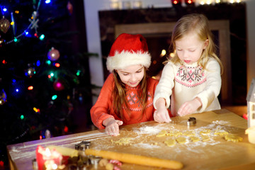 Two adorable little sisters baking Christmas cookies by a fireplace