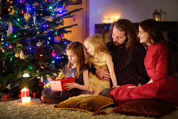 Young happy family of four unwrapping Christmas gifts by a fireplace