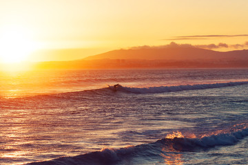 Obraz premium Surfer with surfboard on Atlantic ocean waves on the beach at sunset, Portugal