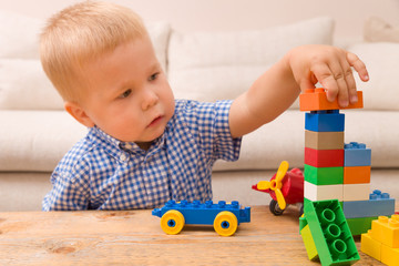 Portrait of child playing with colorful plastic bricks at the table. Toddler having fun and building a train out of constructor bricks. Early learning. Developing toys