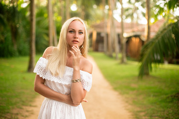 Beautiful blonde woman in white dress posing in the tropical forest - close up portrait