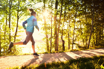 Woman running in park during sunny morning - obrazy, fototapety, plakaty