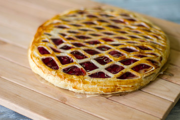 Pie on light wooden surface. Dough with red berries. Delicious cherry pie. Filling of sugar and fruit.