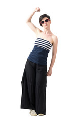 Pretty young woman wearing sunglasses with raised arm and clenched fist. Full body length portrait isolated over white studio background.