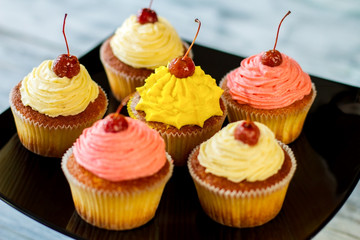 Cupcakes with cherries on top. Pastry on black plate. Sweet treats with different flavors. How to surprise the guests.