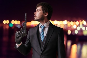 Secret agent or assassin is holding gun with silencer in hand at night.