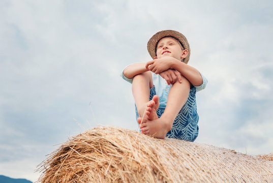 Boy sits on the haystack top with sunny sky background