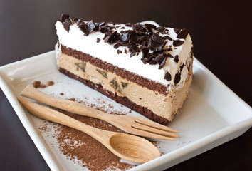 A piece of chocolate cake on square dish with wooden spoon and fork and Chocolate powder