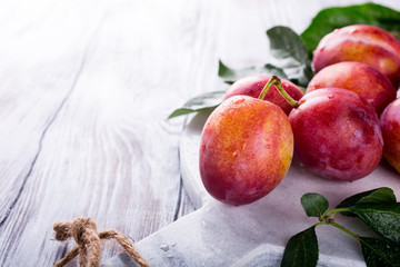 Fresh plums on marble cutting board on old white wooden background. Selective focus. Healthy food concept. Copy space.