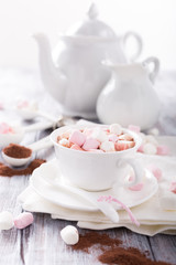 Cup of hot chocolate with mini marshmallows with cocoa on white wooden background.
