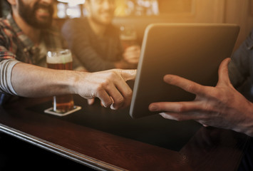close up of men with tablet pc and beer at bar