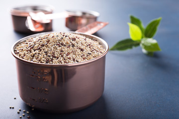 Mixed raw quinoa, South American grain, in copper measuring cup with bay laurel leaves on blue background. Healthy and gluten free food. Copy space.