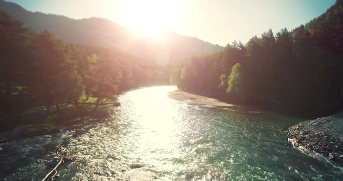 4k (UHD) aerial view. Low flight over fresh cold mountain river at sunny summer morning. Green trees and sun rays on horisont.