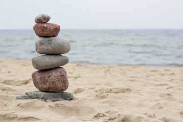 Fototapeta na wymiar Pyramid of the stones on the sandy beach at ocean background