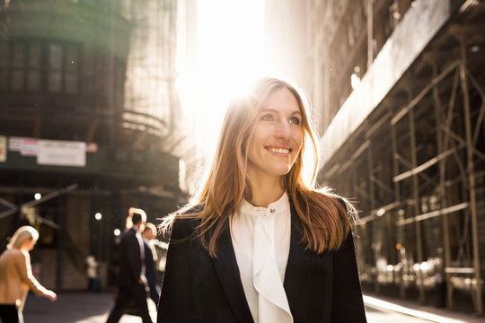 Smiling businesswoman standing on city street during sunny day