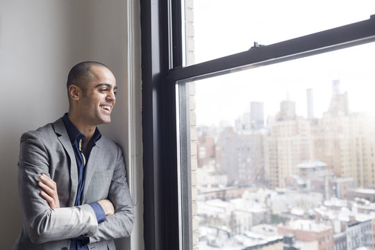 Happy Businessman Standing With Arms Crossed At Glass Window