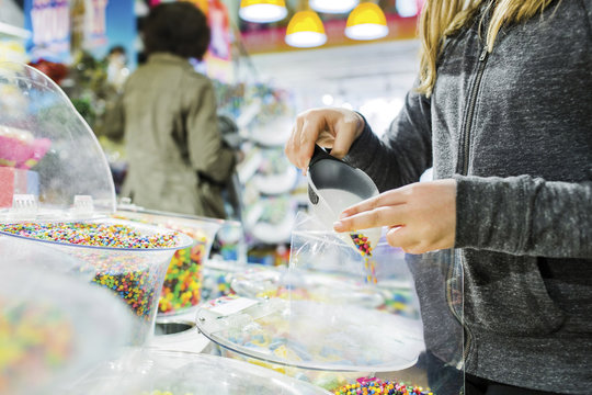 Midsection of girl filling candies in plastic while buying at shop