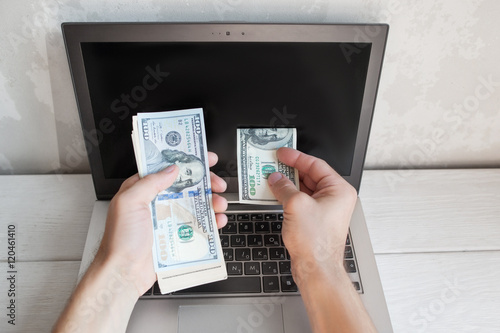 man put dollar bill from batch into laptop blank screen financial waste