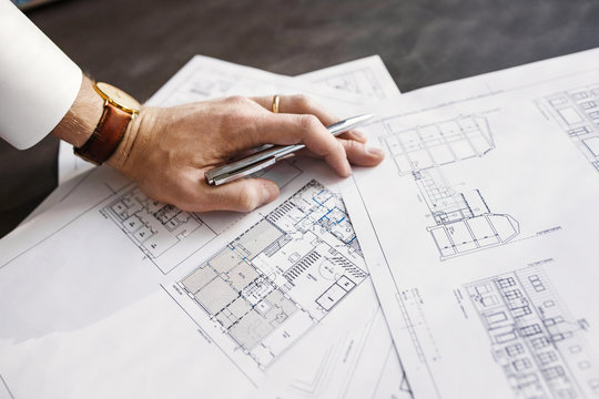 Cropped image architect working on blueprint at table in office