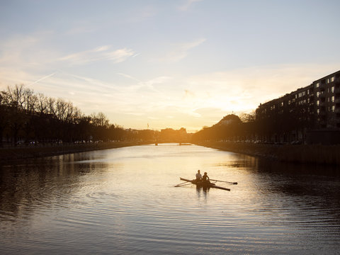 People rowing boat in river during sunset