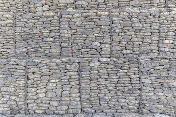 Fototapeta premium The wall of river stones packed in a metal grid