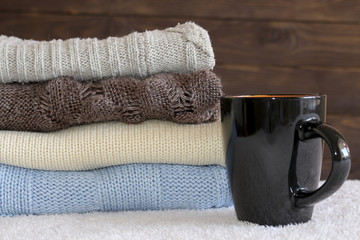 Stack of cozy knitted warm sweater and a mug of coffee . Sweater in retro style.