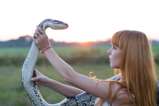 beautiful portrait of a red-haired girl with a snake at sunset   
