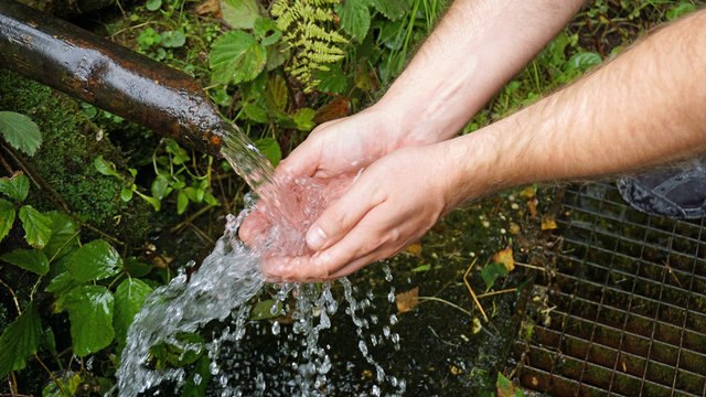 Frisches Quellwasser sprudelt aus einem Rohr in die Hände eines Mannes