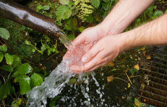Frisches Quellwasser sprudelt aus einem Rohr in die Hände eines Mannes